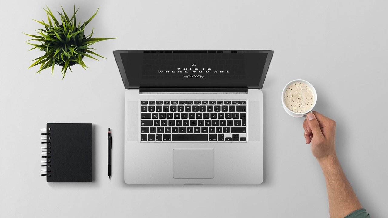 Top view of computer, pen, notebook, plant, coffee